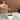 A hand holds a Wildflower Honey Spoon filled with golden wildflower honey above a white cup of tea, with a wooden cutting board and warm wood background.