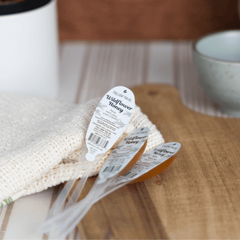 Three Wildflower Honey Spoons filled with golden wildflower honey, resting on a cream knit cloth over a wooden cutting board.