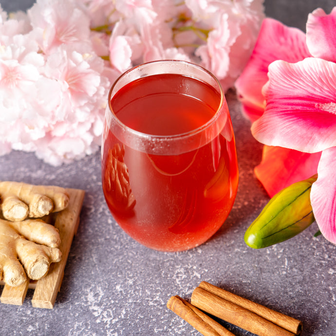 Glass of Blood Pressure Tea with ginger, cinnamon sticks, and pink flowers on a stone surface.