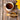 A white mug of brewed Organic Burdock Root Tea on a wooden coaster, with a wooden bowl of burdock root pieces and a Full Leaf Tea Co. spoon in front, and bright yellow flowers on the side.