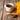A white speckled mug of brewed Organic Burdock Root Tea on a wooden coaster, with a wooden bowl of burdock root pieces and a Full Leaf Tea Co. spoon in front, and bright yellow flowers on the side.