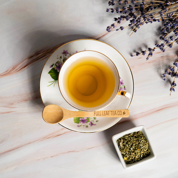 Tea cup with saucer, wooden spoon, and lavender on a marble surface with 'Full Leaf Tea Co.' branding.