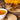 Wooden spoon and bowl filled with chaga mushroom chunks on a wooden board beside a cup of chaga tea and cinnamon sticks.