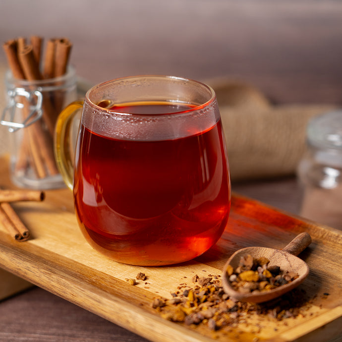 Glass mug of chaga mushroom tea on a wooden tray with cinnamon sticks and a wooden spoon.