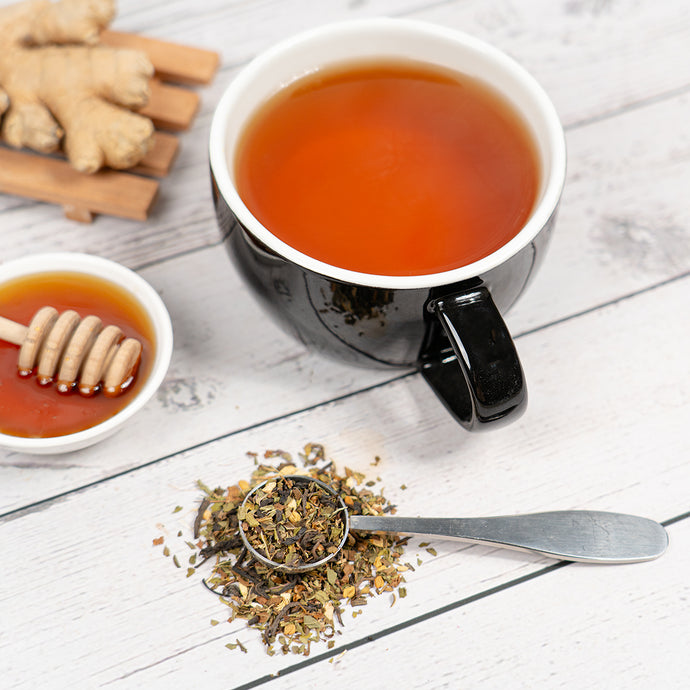 Black mug of cholesterol control tea with honey, ginger, and tea leaves on a wooden surface