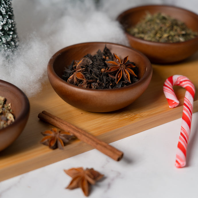 Wooden bowls with dried herbs and spices on a wooden board with a candy cane and cinnamon stick.