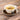 A white teacup filled with clove tea and a tea bag labeled “Inspiring Tea,” sitting on a saucer surrounded by whole cloves on a wooden surface.