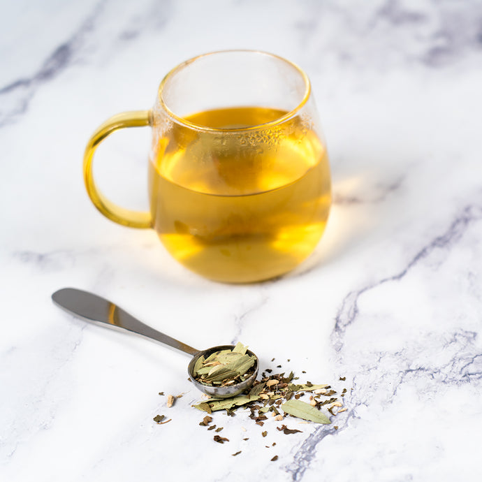 Glass mug of constipation relief tea with dried herbs on a marble surface