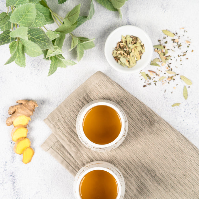 Two cups of constipation relief tea on a textured surface with herbs and spices around