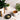 White mug with constipation relief tea, black bowl with tea leaves, and potted plants on a light surface