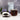 Clear glass mug filled with elderberry tea, surrounded by a bowl of black tea leaves and purple flowers on a wooden surface.