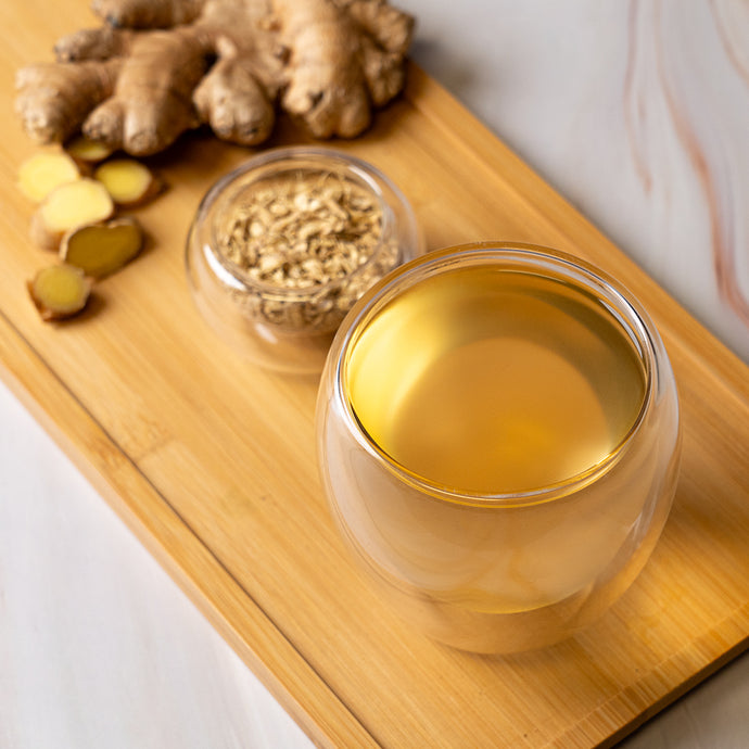 Glass of ginger tea on a wooden tray with fresh ginger roots and ground ginger.