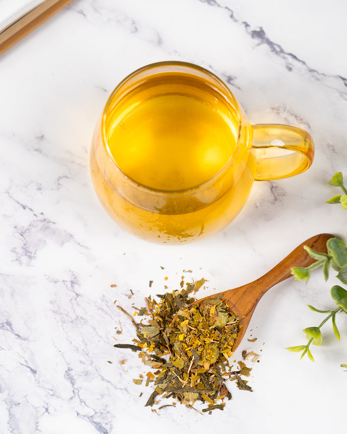 Clear glass mug with healthy vision tea, wooden spoon with dried healthy vision tea on a marble surface.