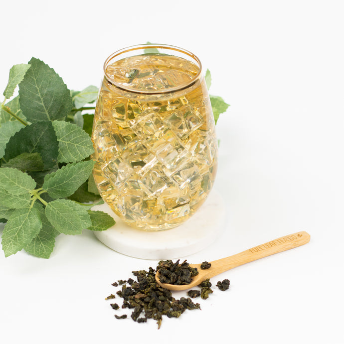Glass of iced tea with tea leaves and a wooden spoon on a white background