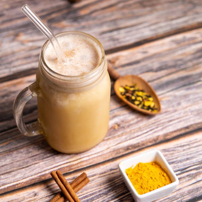 Mason jar with iced cocoa spice circulation latte on a wooden surface with spices and a spoon.