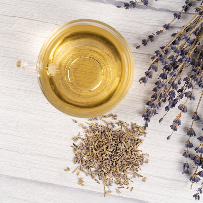 Glass of lavender tea with dried lavender flowers on a light wooden surface