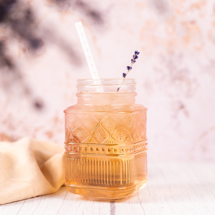 Decorative glass jar with a straw and lavender sprig on a soft background