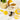 A floral teacup filled with lemon balm tea on a matching saucer, surrounded by fresh lemon slices, a yellow tea infuser, and loose lemon balm leaves on a marble surface.