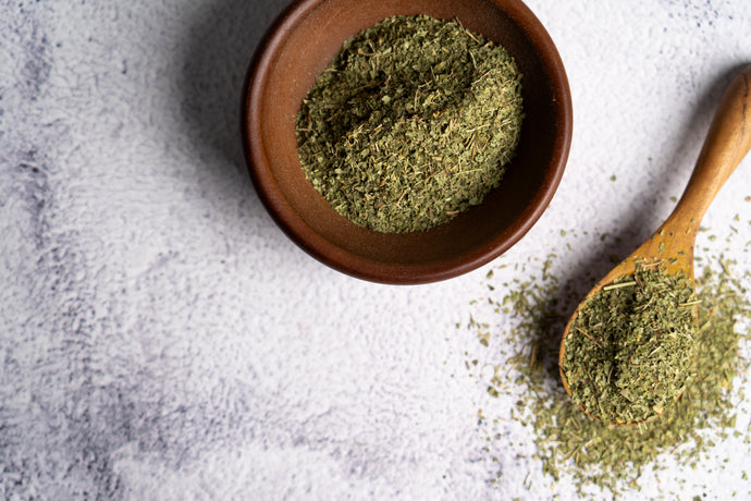 Bowl and wooden spoon filled with Lemon Verbena on a textured surface