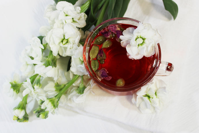 A glass cup of Organic Passion Tea resting on a white cloth with fresh white flowers arranged around it.