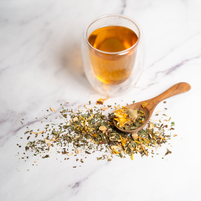 Glass of tea with a wooden spoonful of dried herbs on a marble surface