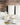 Two white ceramic cups of herbal tea beside a teapot, a bowl of dried mullein leaves, and a spoon on a marble surface, with white canisters and dried lavender in the background.