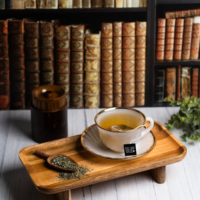 Tea cup with saucer on a wooden tray in front of a bookshelf