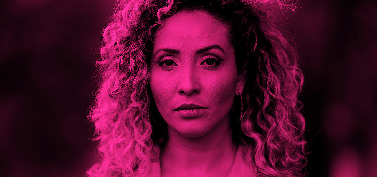 Woman with curly hair under pink light on a dark background.