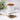 White cup of tea on a white saucer with tea leaves and a spoon on a light surface.