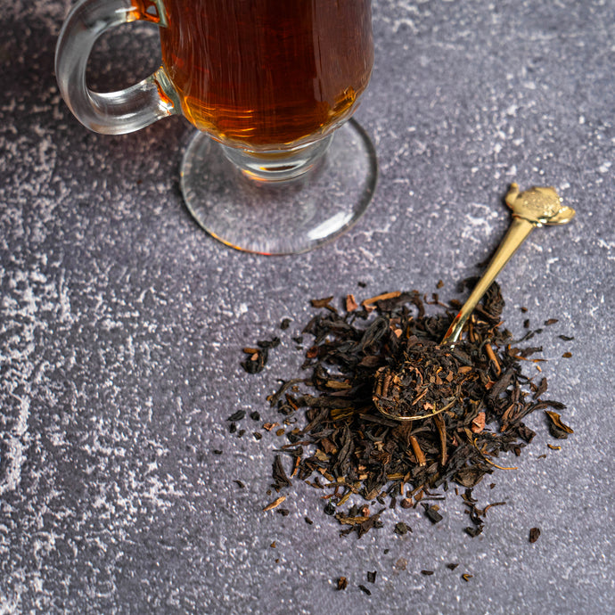 Glass mug of dark liquid next to a pile of tea leaves on a textured surface