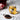 Glass cup of Organic Schisandra Berry tea with a heart design, beside a small dish of dried black Schisandra berries on a marble surface.