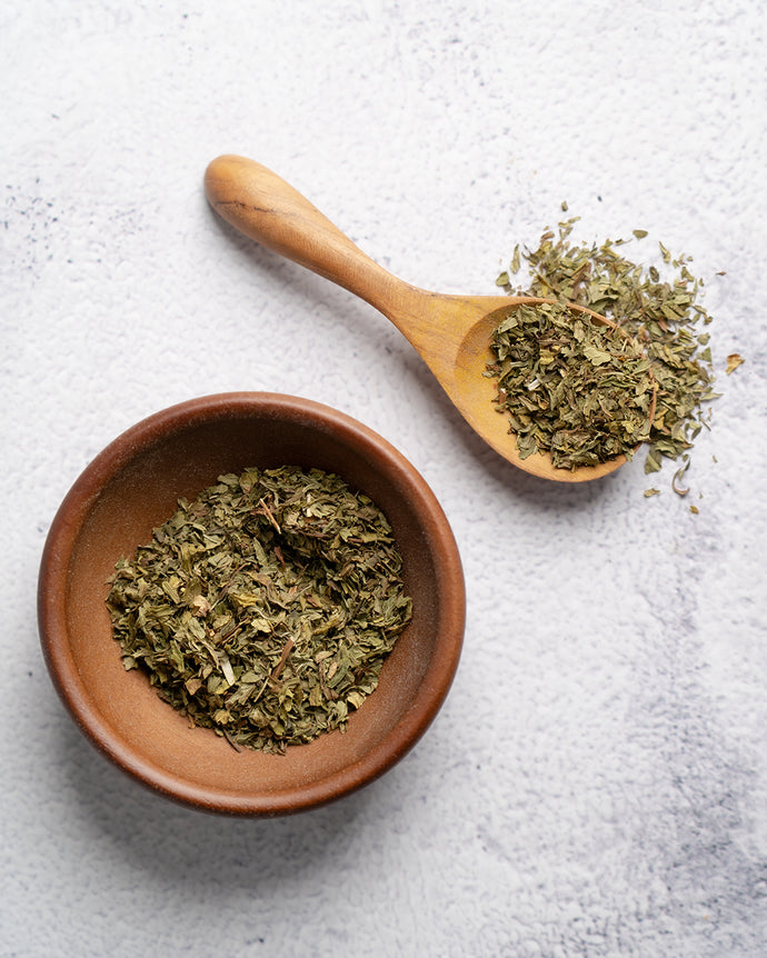 Spearmint herbs in a wooden spoon and bowl on a light gray background