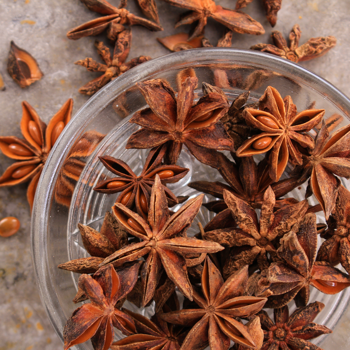 Star anise pods in a glass bowl on a textured surface