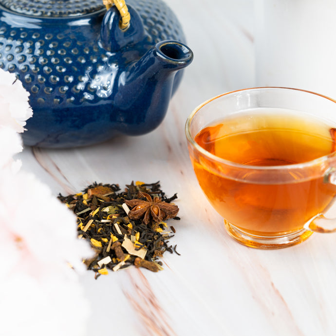 Blue teapot, glass cup with tea, and scattered Thai tea leaves on a white surface