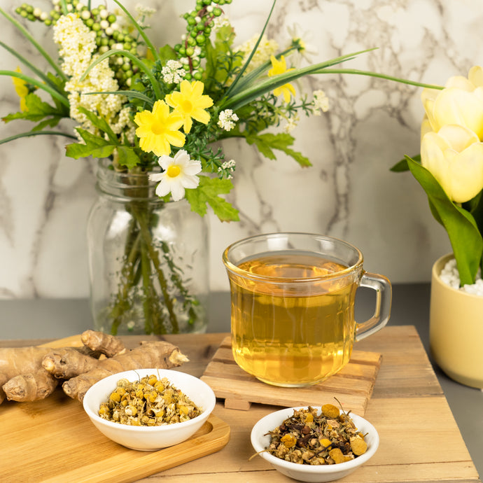 Tea cup with throat clarity tea on a wooden board with flowers and ginger root in the background.