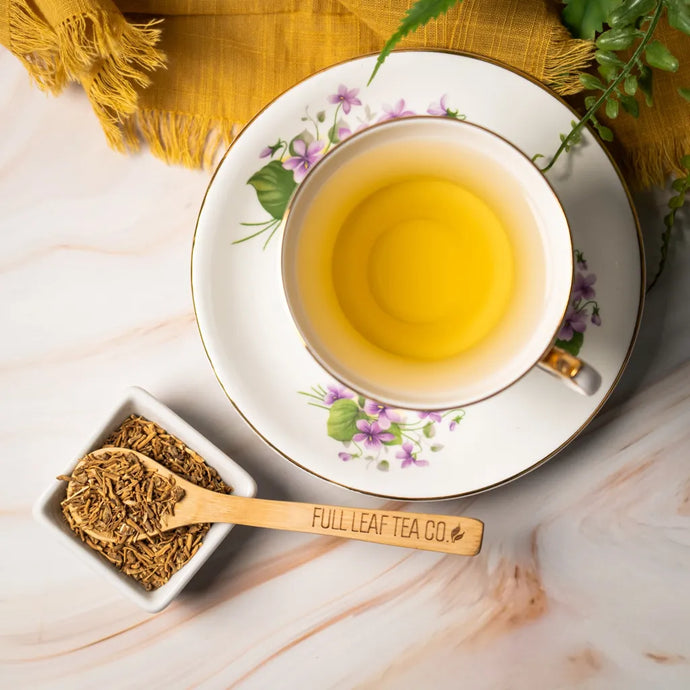 Tea cup with floral design on a saucer, accompanied by a small dish of valerian root and a wooden scoop labeled 'Full Leaf Tea Co.' on a light wooden surface.