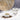 Cardamom pods in a small white dish surrounded by loose seeds beside a glass of clear tea on a marble surface.