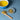 Cup of chamomile tea in a blue mug with dried chamomile flowers on a spoon and small dish on a blue surface.