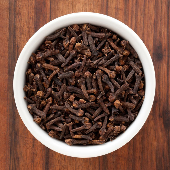 White bowl filled with cloves on a wooden surface