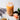 Glass of iced green rooibos spring bliss tea with a creamy orange hue, topped with ice cubes, placed on a light marble surface beside a pink rose, dried tea leaves in a small dish, and sprigs of lavender.