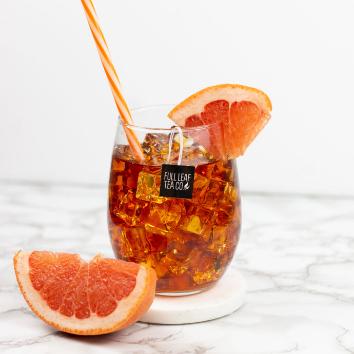 Glass of iced tea with a grapefruit wedge and straw on a marble surface, featuring Full Leaf Tea Co. branding.