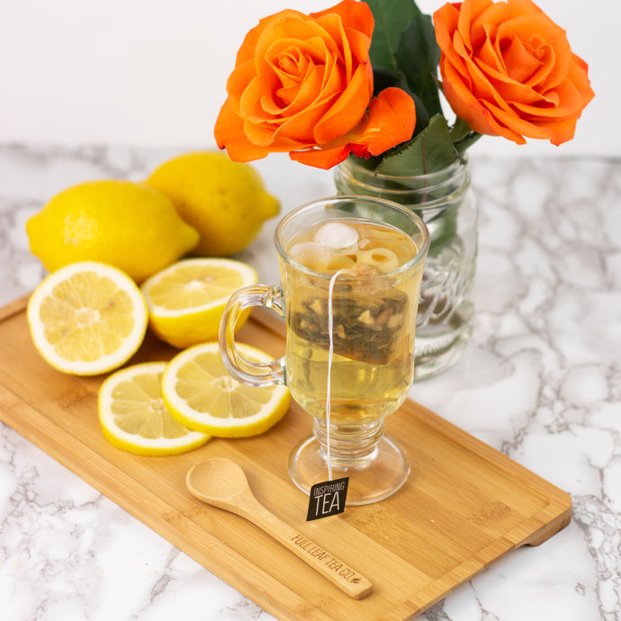 Clear glass mug with tea, wooden spoon, lemons, and orange roses on a marble surface