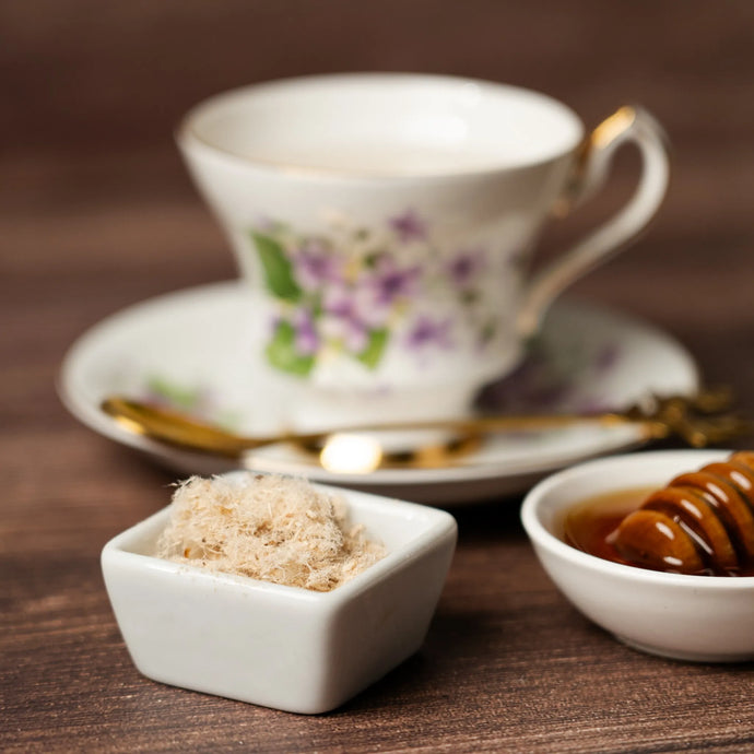 Teacup with floral design on a wooden table, accompanied by a small bowl of slippery elm and a bowl of honey.