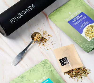 Full Leaf Tea Co. organic loose leaf tea with a black tea infuser, metal teaspoon of herbs, tea bag, and green pouch labeled Organic Liver Cleanse.