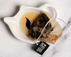 Used Full Leaf Tea Co. tea bag resting in a white ceramic tea bag rest with a small pool of brewed tea.