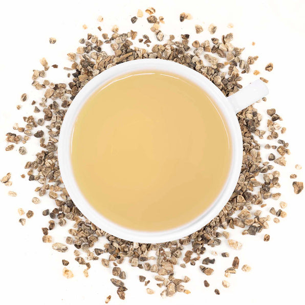 A cup of brewed Organic Devil's Claw tea with dried pieces of the root scattered around.