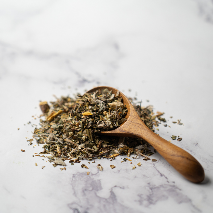 A wooden spoon filled with loose-leaf Organic Allergy Relief Tea blend, featuring dried herbs and botanicals on a light marble surface.