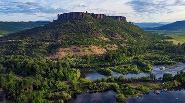 Aerial view of Table Rock in Southern Oregon surrounded by lush green forests, rivers, and open fields under a partly cloudy sky.