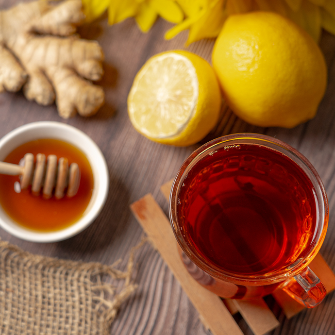 Cup of Organic Immunity Blend tea with honey, lemon, and fresh ginger on a rustic wooden surface, evoking warmth and natural wellness.