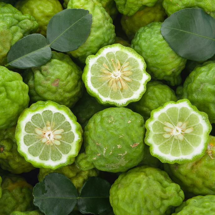 Fresh limes with dark green leaves, including whole and halved fruits showing their textured rind and juicy interior.
